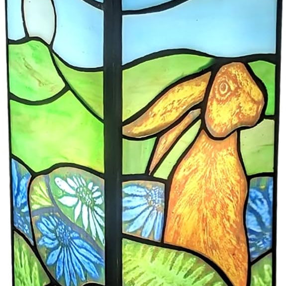 A square Tiffany-style lamp with a black base and a stained glass panel featuring a rabbit design, set against a backdrop of a pastoral landscape with flowers.