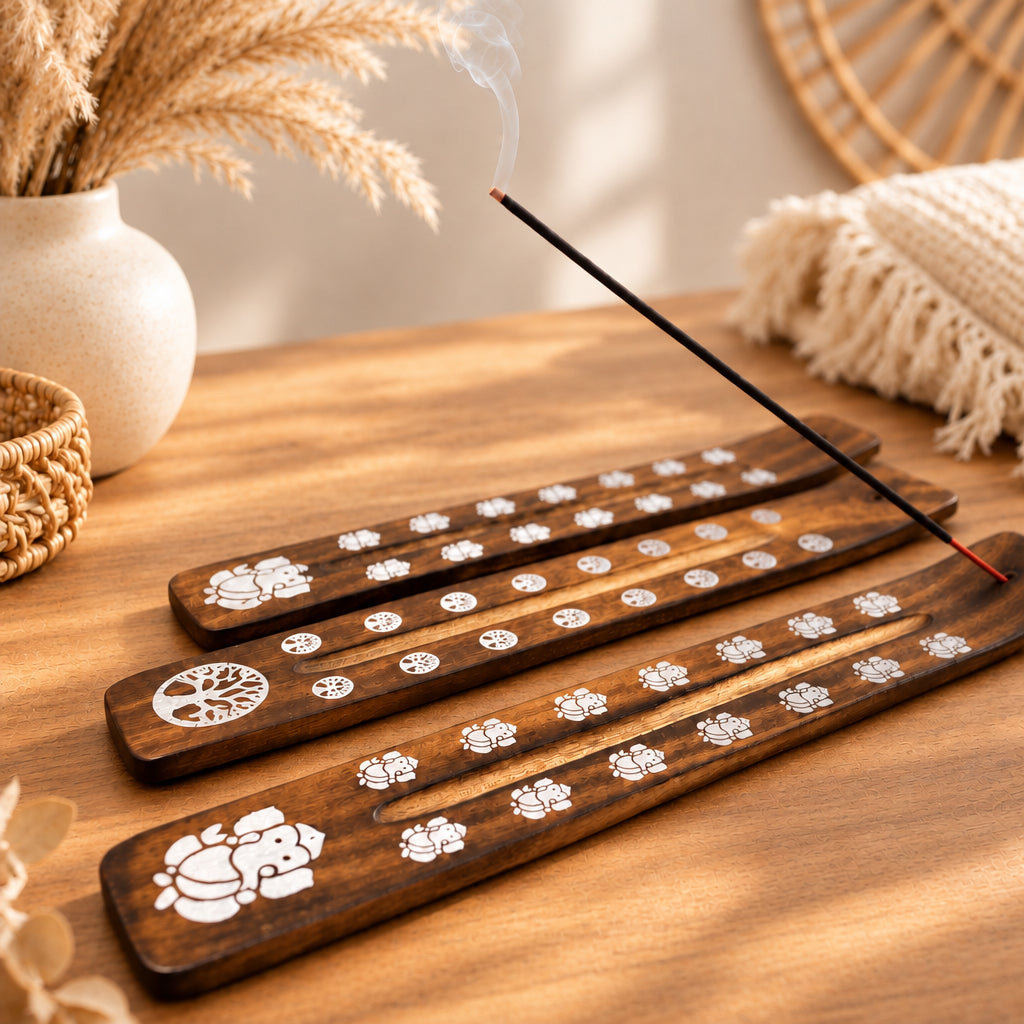 Wooden incense sticks with tree of life designs on a wooden surface, with a blurred statue and plant in the background.