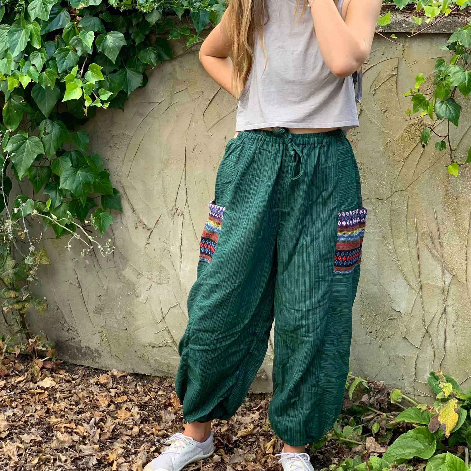 A person standing outdoors wearing green harem trousers with Thai weave pockets and a white top.