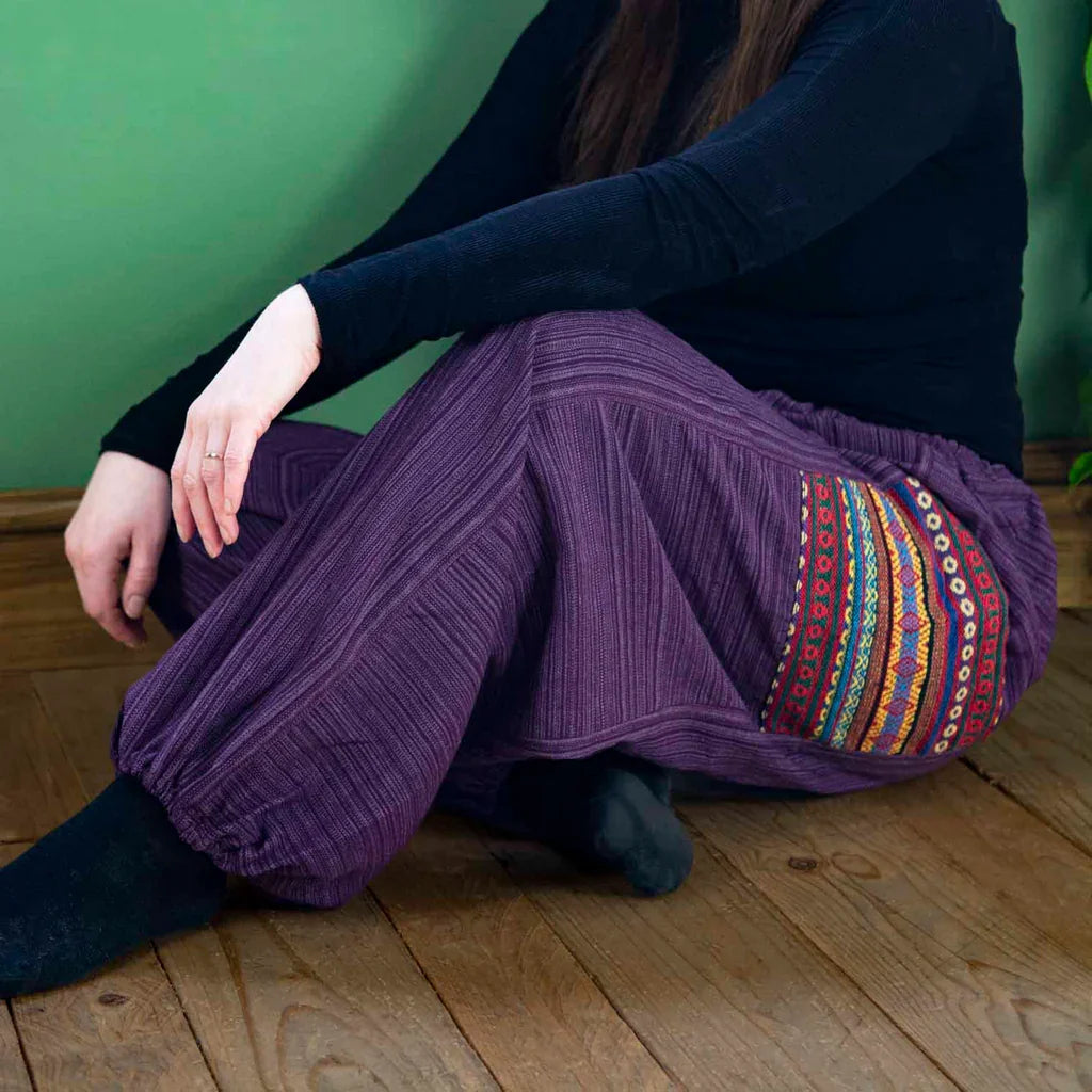 A person wearing purple harem pants with colourful decorative weaving 