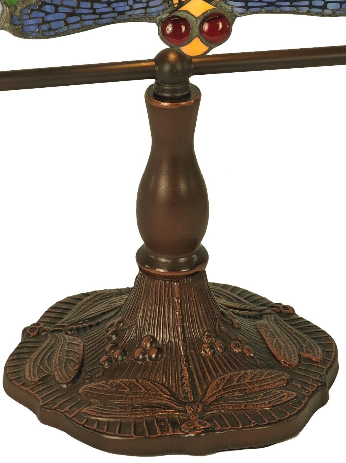 Close-up of a decorative table lamp base and stem in a dark bronze finish, with a stained-glass wing detail showing blue, yellow, and red accents at the top, on a white background.