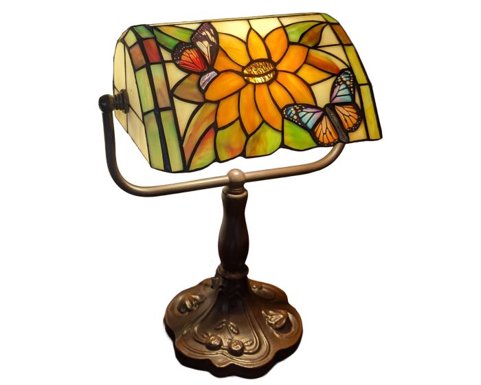 A Tiffany-style stained glass desk lamp featuring a large yellow-orange flower and two butterflies on a cream and green background, mounted on an ornate bronze-colored metal stand with a decorative base.