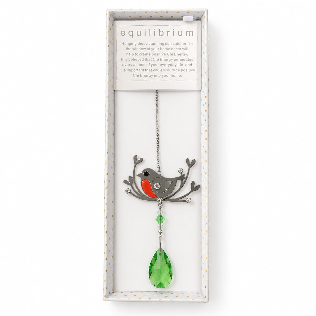 A hanging bird charm pendant displayed inside a long white gift box. The charm features a silver-toned branch and bird silhouette with a red-orange breast and gray wings, hanging from a silver chain with a large green faceted teardrop crystal at the bottom.