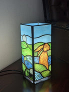 Rabbit design square Tiffany table lamp illuminated with stained glass depicting a hare in a field | stained glass