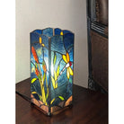 Decorative lamp with stained glass design featuring flowers and a dragonfly on a wooden surface.