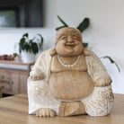 Wooden laughing Buddha statue on a wooden surface with a blurred indoor background
