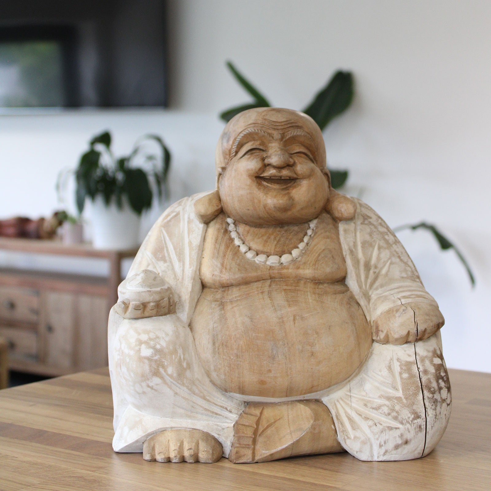 Wooden laughing Buddha statue on a wooden surface with a blurred indoor background